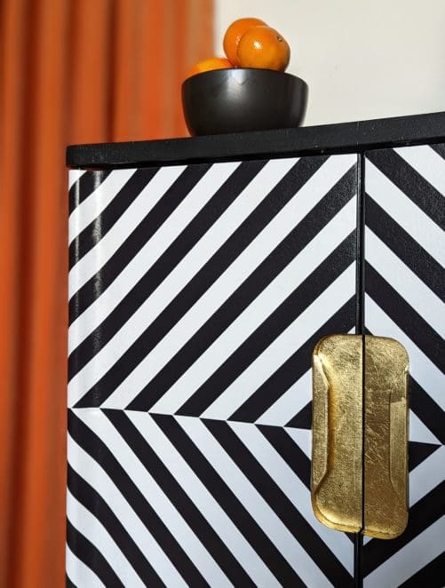 Close up view of gold leaf recessed handles to black and white op-art style cabinet doors