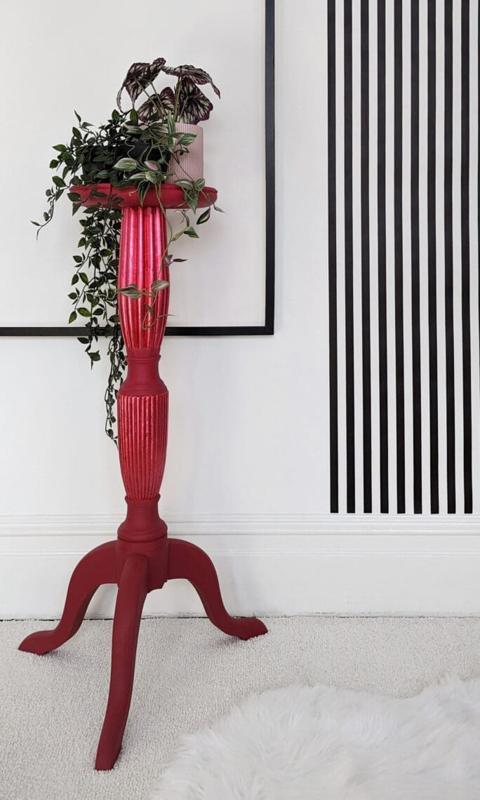 Tall red plant stand with trailing plants and black and white striped wall