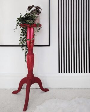 Tall red plant stand with trailing plants and black and white striped wall