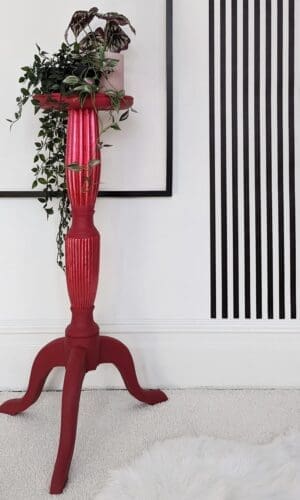 Tall red plant stand with trailing plants and black and white striped wall