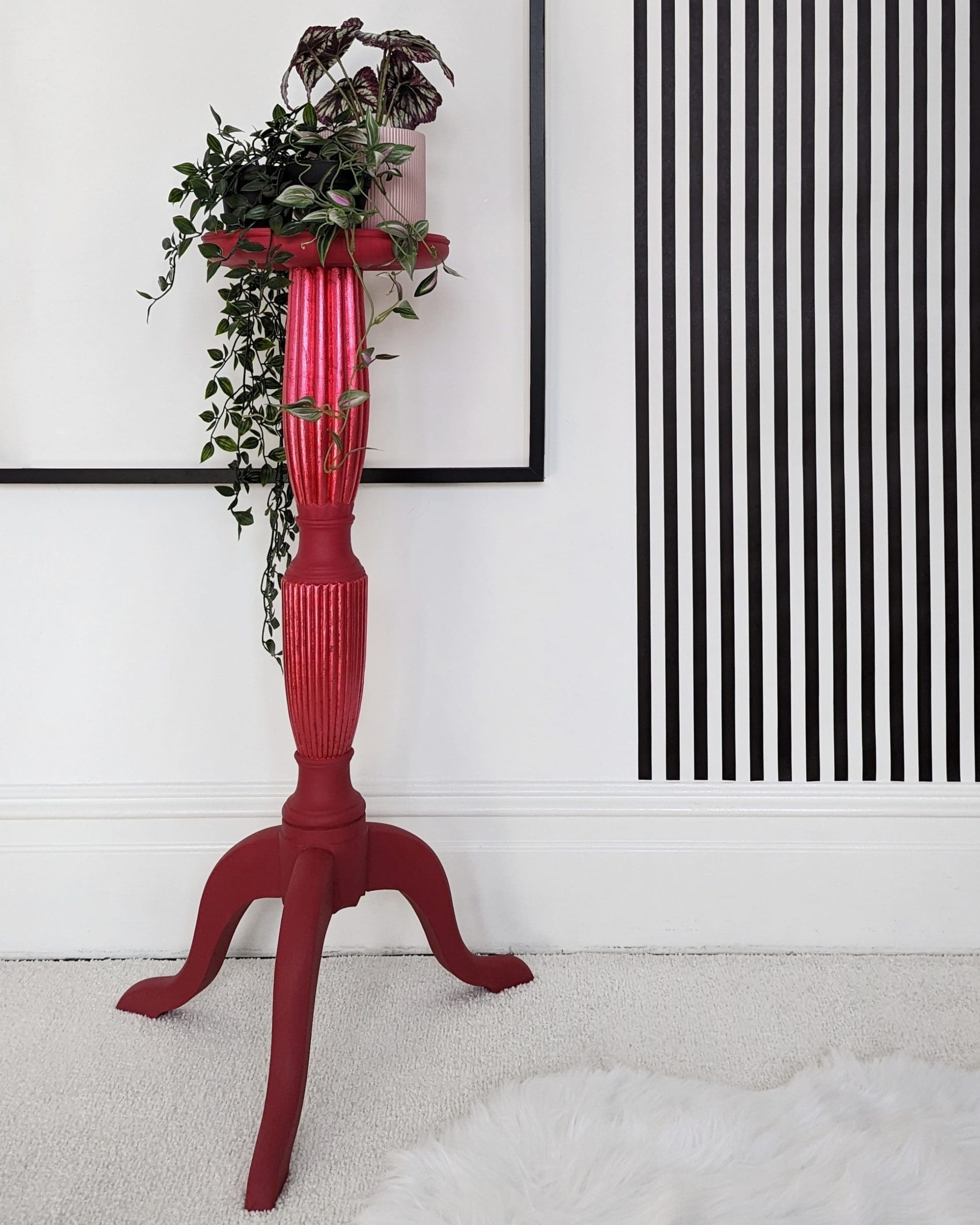 Tall red plant stand with trailing plants and black and white striped wall