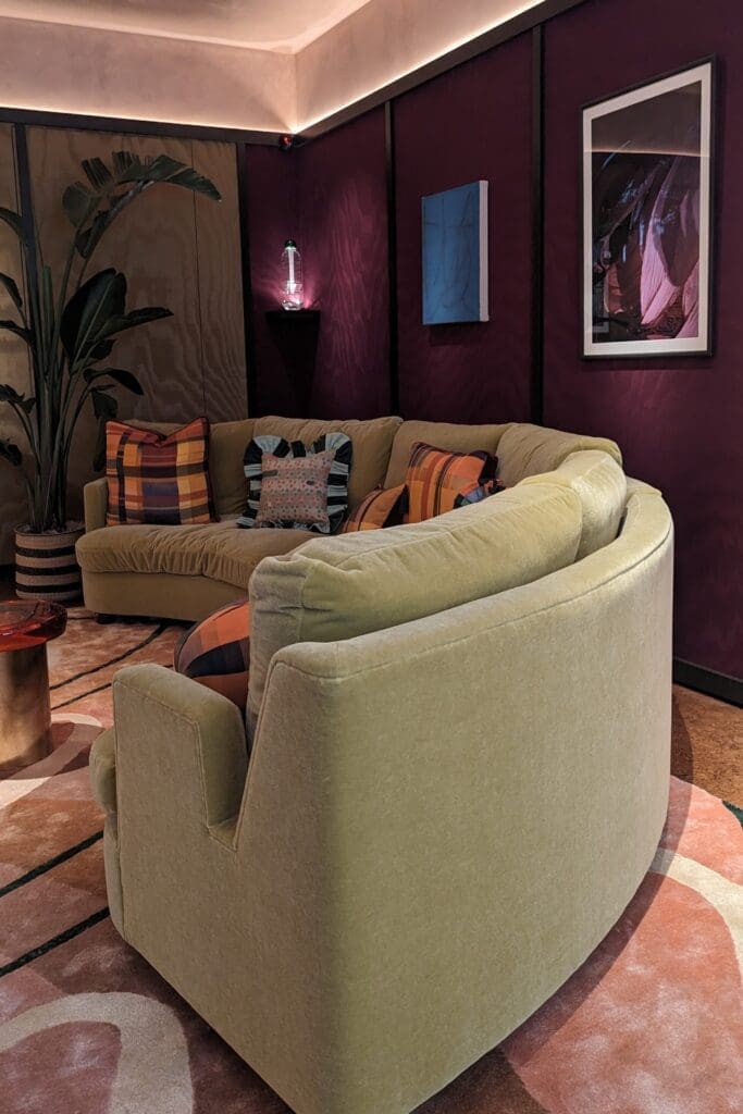 Green velvet curved sofa against plum coloured silk clad walls