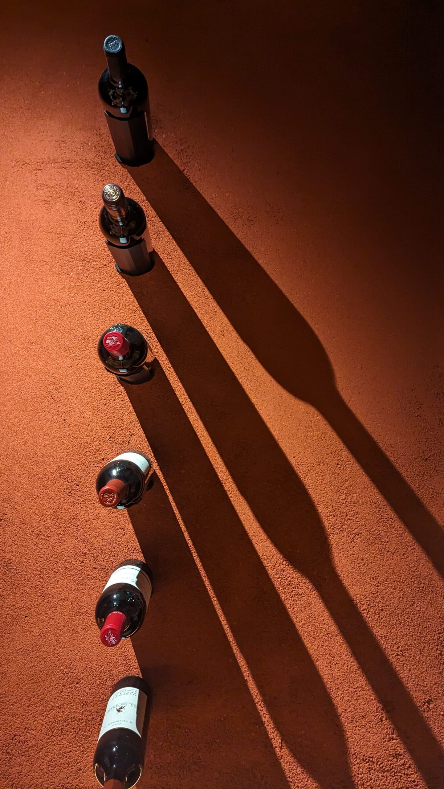 Wine bottles casting shadows on a terracotta wall