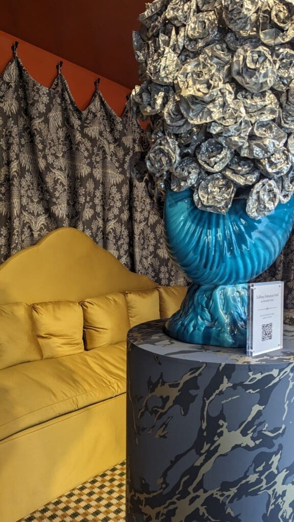 Yellow sofa behind a turquoise vase on a mabled plinth