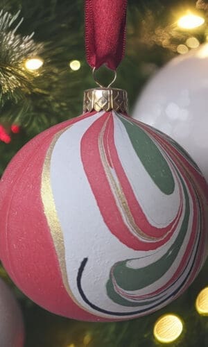 Red, gree, black, white and gold marbled bauble hanging on Christmas tree with fairy lights and white baubles