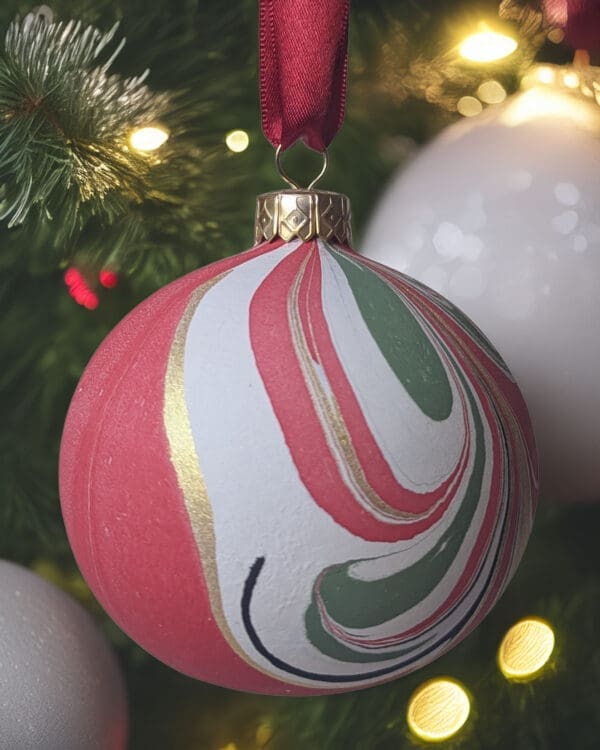 Red, gree, black, white and gold marbled bauble hanging on Christmas tree with fairy lights and white baubles