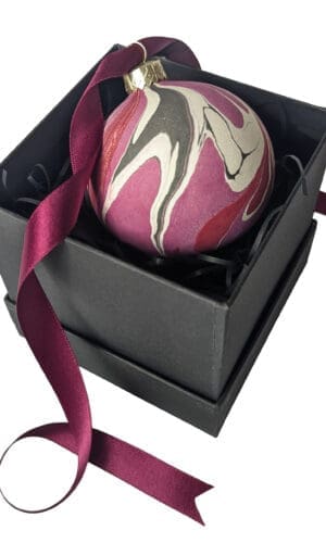 Marbled ceramic Christmas bauble in reds and purples in a black gift box with a curly dark red ribbon