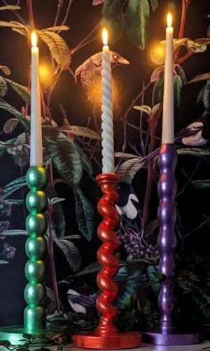 Orange, green and purple barley twist candlesticks on a mantlepiece with a dark floral background