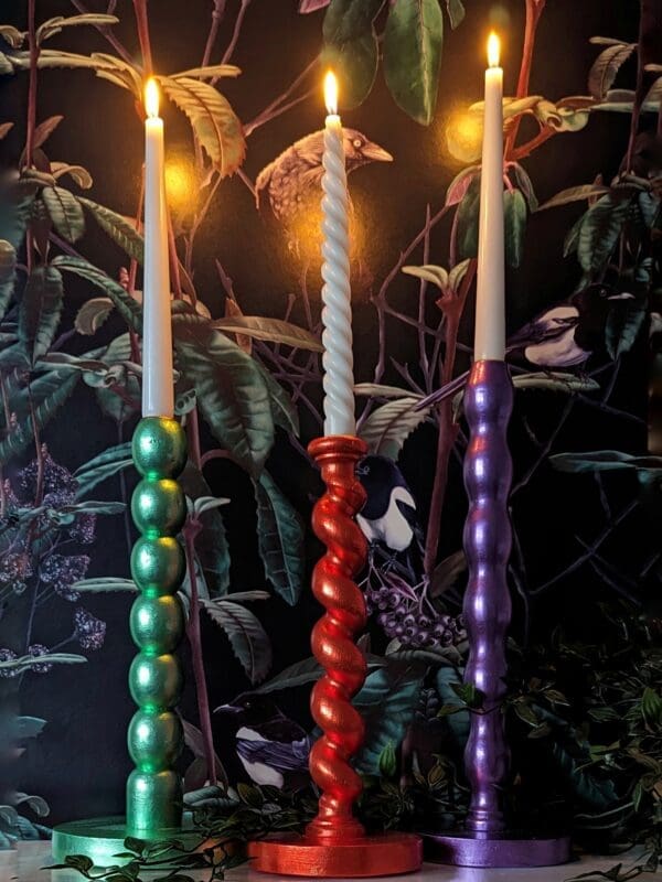 Orange, green and purple barley twist candlesticks on a mantlepiece with a dark floral background