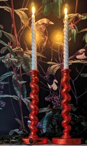 Orange barley twist candlesticks on a mantlepiece with a dark floral background