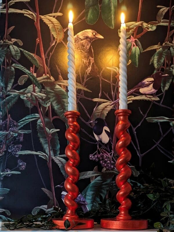 Orange barley twist candlesticks on a mantlepiece with a dark floral background