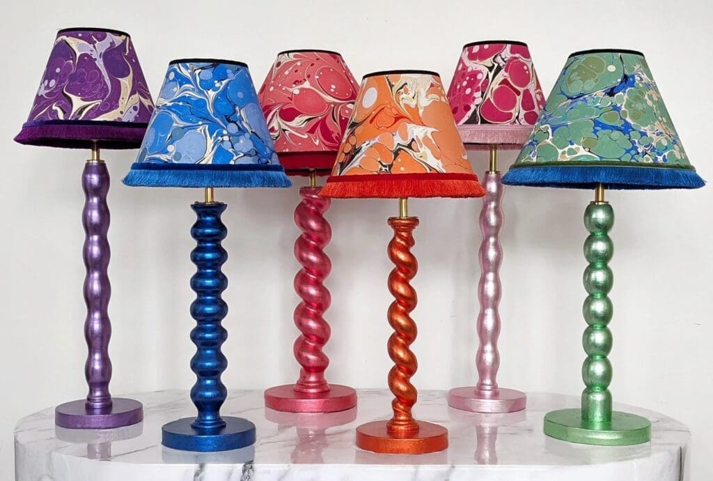 lamps on marble plinth colourful metallic lamps in barley twist and bobbin style in purple, blue, red, orange, pink and green with matching marbled lampshades with fringe trim.