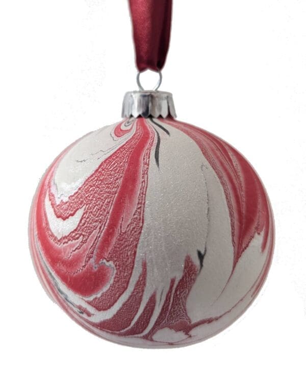 marbled christmas bauble in red and pink and pearlescent white hanging on a red ribbon